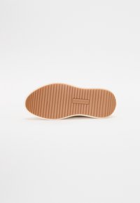 Suola di sneaker bianca con una base in gomma marrone texturizzata e rigata. Presenta un piccolo logo e un bordo liscio, adatta per un abbigliamento casual.