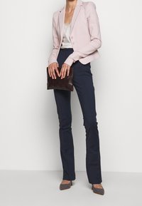Blazer ajustado de color rosa claro, pantalones de corte elegante en azul marino y un clutch de tejido oscuro. Unos tacones puntiagudos con un patrón texturizado complementan el look.