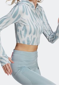 Femme portant un crop hoodie zippé à motifs bleu clair et un legging taille haute bleu clair uni dans une pose active.