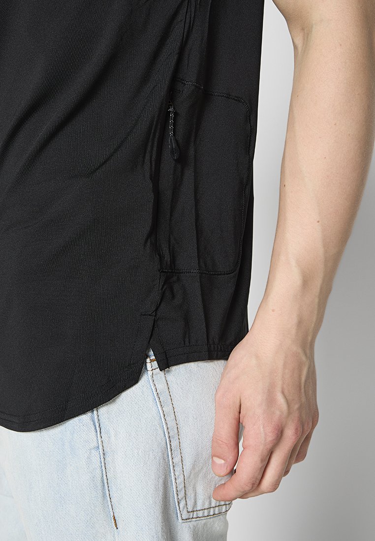 Schwarzes kurzärmeliges T-Shirt mit einer Seitentasche, strukturiertem Stoff und abgerundetem Saum, kombiniert mit hellblauen Jeans.