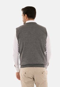 Gilet grigio a maglia con collo rotondo, design senza maniche e orlo a costine, indossato sopra una camicia bianca a maniche lunghe, visto da dietro.