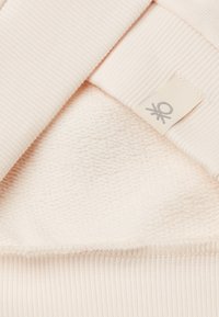 Strati di tessuto rosa chiaro: una texture a coste sopra e una base morbida simile a un asciugamano. Include un piccolo etichetta con un logo grigio.