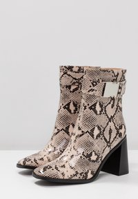 Stivali alla caviglia in pelle di serpente beige e nera, con punta affusolata, tacco a blocco e un accento in metallo argentato sulla cinghia alla caviglia.