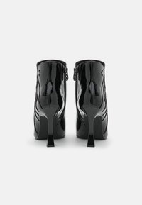 Bottines en cuir verni noir avec un bout pointu, de hauts talons aiguilles, des zips latéraux et des lignes courbes subtiles le long des côtés.