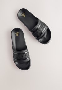 Sandali neri con design testurizzato, dotati di doppie fasce spesse e un sottile motivo geometrico sulla parte superiore. Finitura liscia, branding minimale.