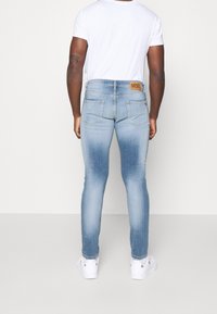 Jeans de mezclilla de corte ajustado en tono azul claro con una textura desgastada, que cuentan con dos bolsillos traseros y un parche de cuero con marca cerca de la cinturilla.