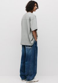Oversized grijze katoenen t-shirt met korte mouwen, gecombineerd met blauwe denim jeans met wijde pijpen en een logo label op de achterzak.