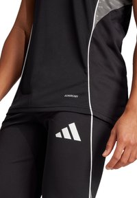 Top sportivo nero con accenti grigi, presenta il logo AEROREADY; abbinato a leggings neri con logo a tre strisce bianche.