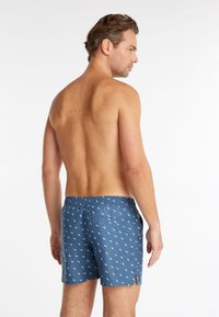 Shorts de bain bleus avec un motif abstrait blanc, taille élastique et poches latérales, vus de dos. Texture lisse.