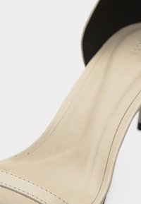 Μπεζ ψηλοτάκουνα σανδάλια ανοιχτής μύτης με λεπτό μαύρο τακούνι και λείο δερμάτινο πέλμα.