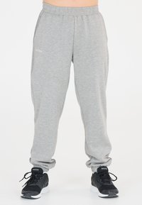 Hellgraue Sweatpants mit elastischem Bund, Bündchen an den Knöcheln und dem aufgestickten Text "Les Ares" auf der Vorderseite. Kombiniert mit schwarzen Sneakers.