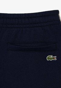 Pantalon de survêtement bleu marine en tissu doux, avec un petit logo crocodile vert brodé et une poche arrière à ouverture ajustée.