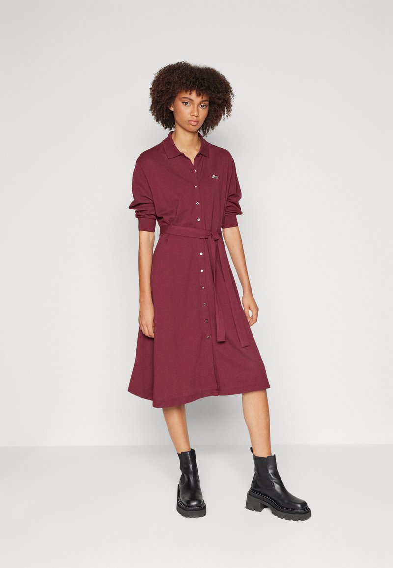 Burgunderfarbendes Hemdkleid mit Gürtel, langen Ärmeln und einer leichten A-Linien-Form. Schwarze Knöchelstiefel mit robusten Sohlen vervollständigen den Look.