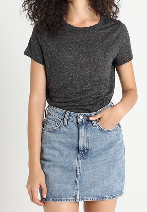 Kvinde iført en mørkegrå kortærmet t-shirt, stukket ned i et lyseblåt højhalset jeansskørt med lommer.