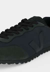 Σκούρο πράσινο και μαύρο sneaker χαμηλού τύπου με υφασμένη κάλυψη στα δάχτυλα, μαύρα κορδόνια και ένα στυλιζαρισμένο λογότυπο "V" στο πλάι.
