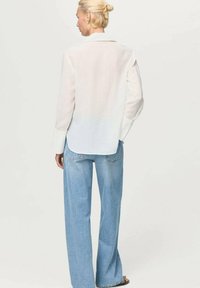Weißes Langarmhemd mit weicher Textur, offenem Kragen und geknöpften Manschetten, kombiniert mit hellen weiten Jeans. Rückansicht.
