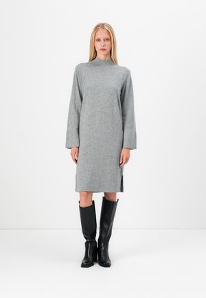 Robe en tricot grise à manches longues, col haut et fentes latérales, associée à des bottes noires en cuir hautes. Texture lisse et design minimaliste.