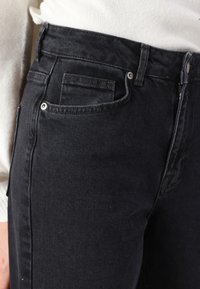 Black denim jeans featuring a fitted design, five pockets, subtle stitching, and standard button and zipper closure. Soft texture with slight stretch.