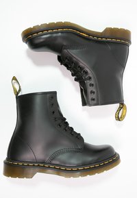 Svarta läderankelstövlar med en slät yta, prydda med gula sömmar, en tjock gummisul och en dragflik på hälen.