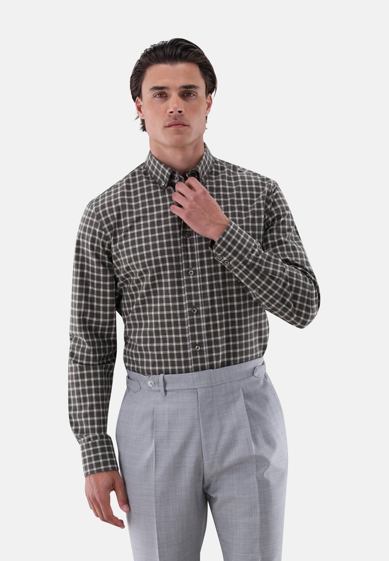 Button-up Hemd in olivgrün mit weißem Karomuster, langärmlig und mit Kragen; graue plissierte Hosen mit seitlichen Laschen.