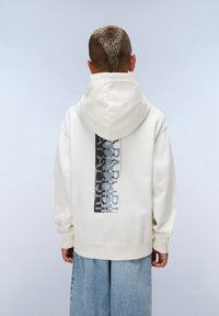 Hoodie crème avec un imprimé graphique gris et noir au dos, doté d'une capuche à cordon et de poignets côtelés. Porté avec un jean large bleu clair.