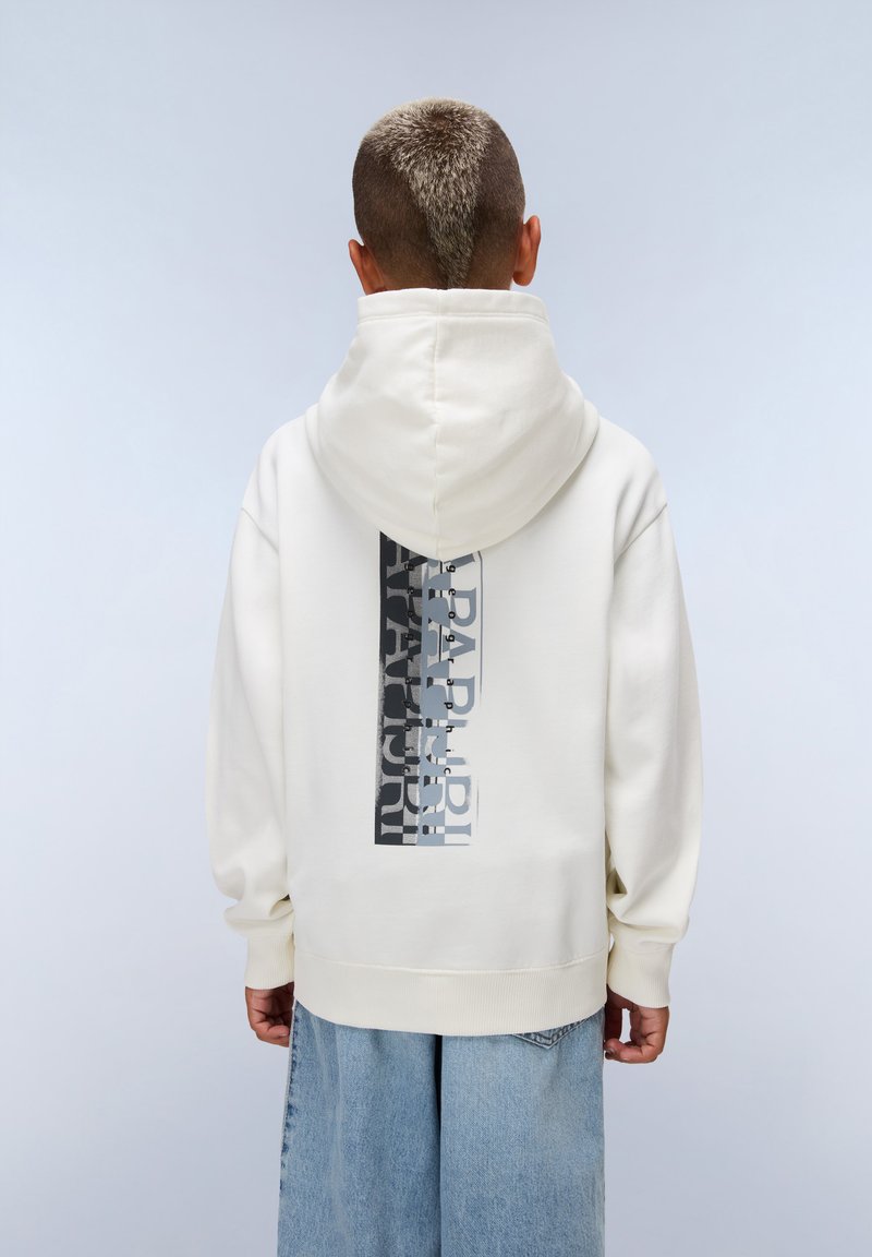Hoodie crème avec un imprimé graphique gris et noir au dos, doté d'une capuche à cordon et de poignets côtelés. Porté avec un jean large bleu clair.