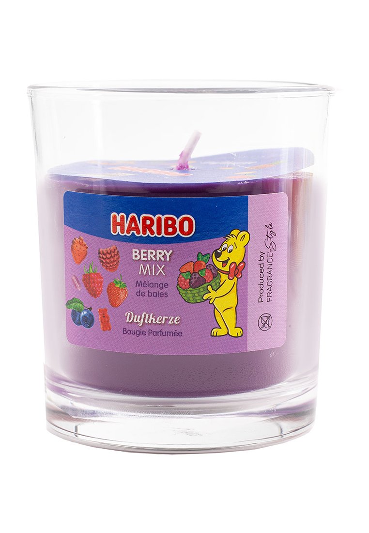 Vela aromática morada en un recipiente de vidrio transparente. La etiqueta presenta un oso de dibujos animados con frutas, que dice "Haribo Berry Mix". Mecha expuesta en la parte superior.