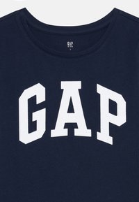 T-shirt bleu marine en coton avec un col rond côtelé, présentant un grand logo "GAP" blanc en lettres majuscules.
