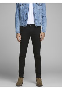 Jeans ajustados negros, mezcla de algodón, de cintura alta, con diseño de cinco bolsillos, silueta ajustada y ligero estiramiento. Llevados con una chaqueta de mezclilla.