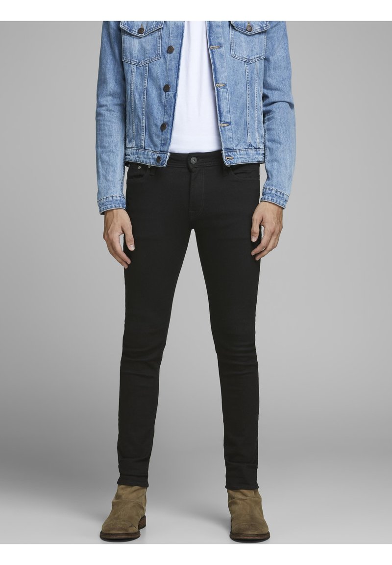 Jeans ajustados negros, mezcla de algodón, de cintura alta, con diseño de cinco bolsillos, silueta ajustada y ligero estiramiento. Llevados con una chaqueta de mezclilla.