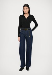 Zwarte langarmige poloshirt met knopen, gecombineerd met high-waisted wijde donkerblauwe denim jeans en een zwarte riem met goudkleurige gesp. Zwarte enkellaarzen.