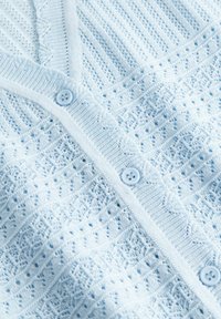 Lys blå strikket cardigan med intrikate blondermønstre og runde matchende knapper langs fremåpningen.