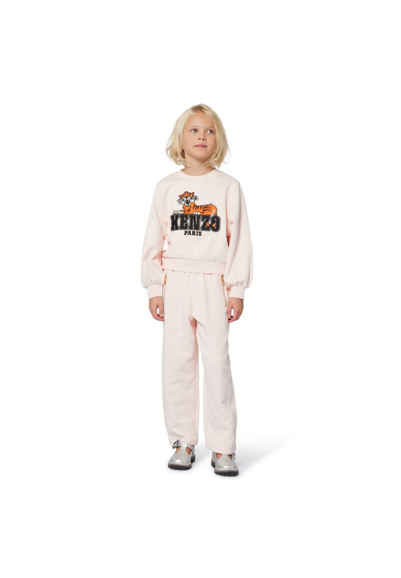 Jasnoróżowy komplet dresowy z grafiką tygrysa i napisem "KENZO PARIS". Bluzka ma bufiaste rękawy; spodnie są luźne i mają sznurek w talii.