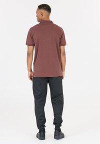 Burgunderröd polo med korta ärmar, platt stickad krage och rak nederkant; kombinerad med svarta joggerbyxor och svarta sneakers.