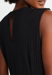 Czarna, teksturowana sukienka z wycięciem w kształcie łezki z tyłu i zapięciem na guziki. Bez rękawów, z marszczoną strukturą materiału.