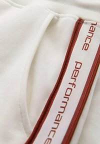 Biała tkanina sportowa z bocznym szwem ozdobionym maroonowym i kremowym paskiem, wyszytym słowem "performance".