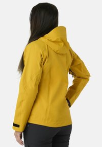 Giacca impermeabile gialla con cappuccio, caratterizzata da un design snodato, tasca laterale con zip e dettagli in Velcro nero sui polsini.