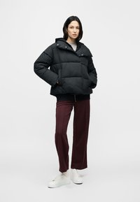 Čierna zateplená prešívaná bunda s kapucňou, s boxy strihom, patentnými gombíkmi a bočnými vreckami, doplnená bordovými nohavicami a bielymi teniskami.