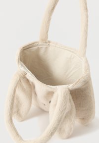 Geantă mică din blană artificială bej, cu mânere moi și urechi lungi pufoase, dotată cu un deschizător în partea de sus care arată o căptușeală interioară simplă.