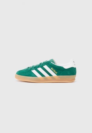 Zelene ante sneakers s bijelim prugama, gumenom potplatom i zlatnim "Gazelle" brandingom. Imaju teksturirani jezik i podstavljeni ovratnik za udobnost.
