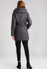 Gray puffer coat with a high collar and a belted waist, featuring chevron quilted texture and long sleeves, worn over black pants.