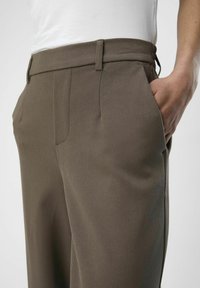 Hnědé kalhoty z texturované tkaniny s přizpůsobeným střihem, bočními kapsami a hladkým pasem. Viditelné švy na švech.