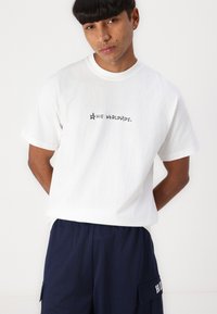 White cotton T-shirt with "HUF WORLDWIDE." printed in black on the front. Short sleeves and a relaxed fit, paired with navy mesh shorts.