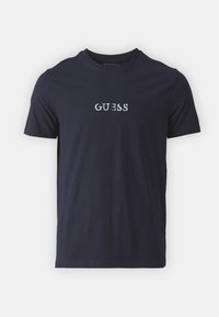 T-shirt de algodón azul marino con manga corta y escote redondo, que presenta el nombre de la marca bordado "GUESS" en blanco en la parte delantera.