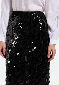 Falda negra de lentejuelas con un diseño ajustado y una superficie texturizada. Las lentejuelas reflejan la luz, creando un efecto brillante.