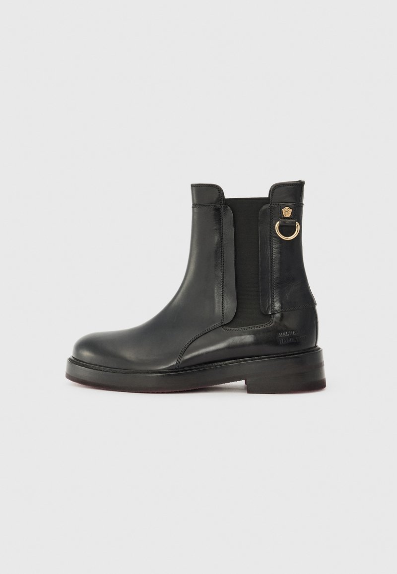 Botim de couro preto até o tornozelo com painéis laterais elásticos, bico arredondado e detalhe em forma de anel dourado. Sola plana com um leve salto e marcação em relevo.