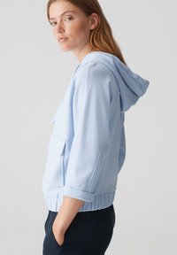 Felpa con cappuccio azzurro chiaro, dotata di tasca frontale, polsini arrotolati e orlo a coste, realizzata in tessuto morbido, con un design informale.