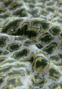 Tessuto astratto in stampa leopardo verde e giallo con una superficie morbida e testurizzata, caratterizzato da uno sfondo bianco trasparente.