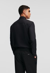 Schwarzes Langarmhemd mit strukturiertem Kragen, aus glattem Stoff und mit Knopfverschlüssen, kombiniert mit schwarzen Pants mit elastischem Bund.