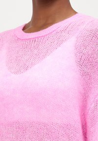 Ljusrosa, genomskinlig stickad tröja med rund halsringning och strukturerat mönster. Tyget är mjukt och något genomskinligt.